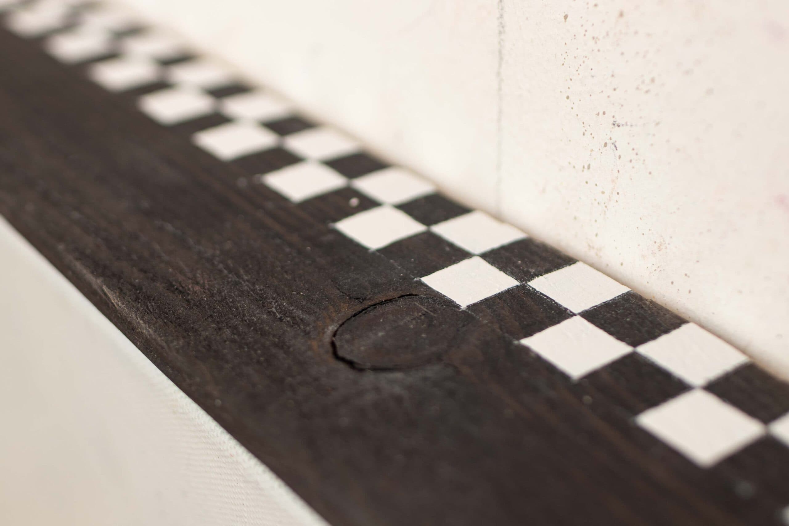Handmade floater frame in matte black with a natural rough wooden surface and subtle checkerboard ribbon